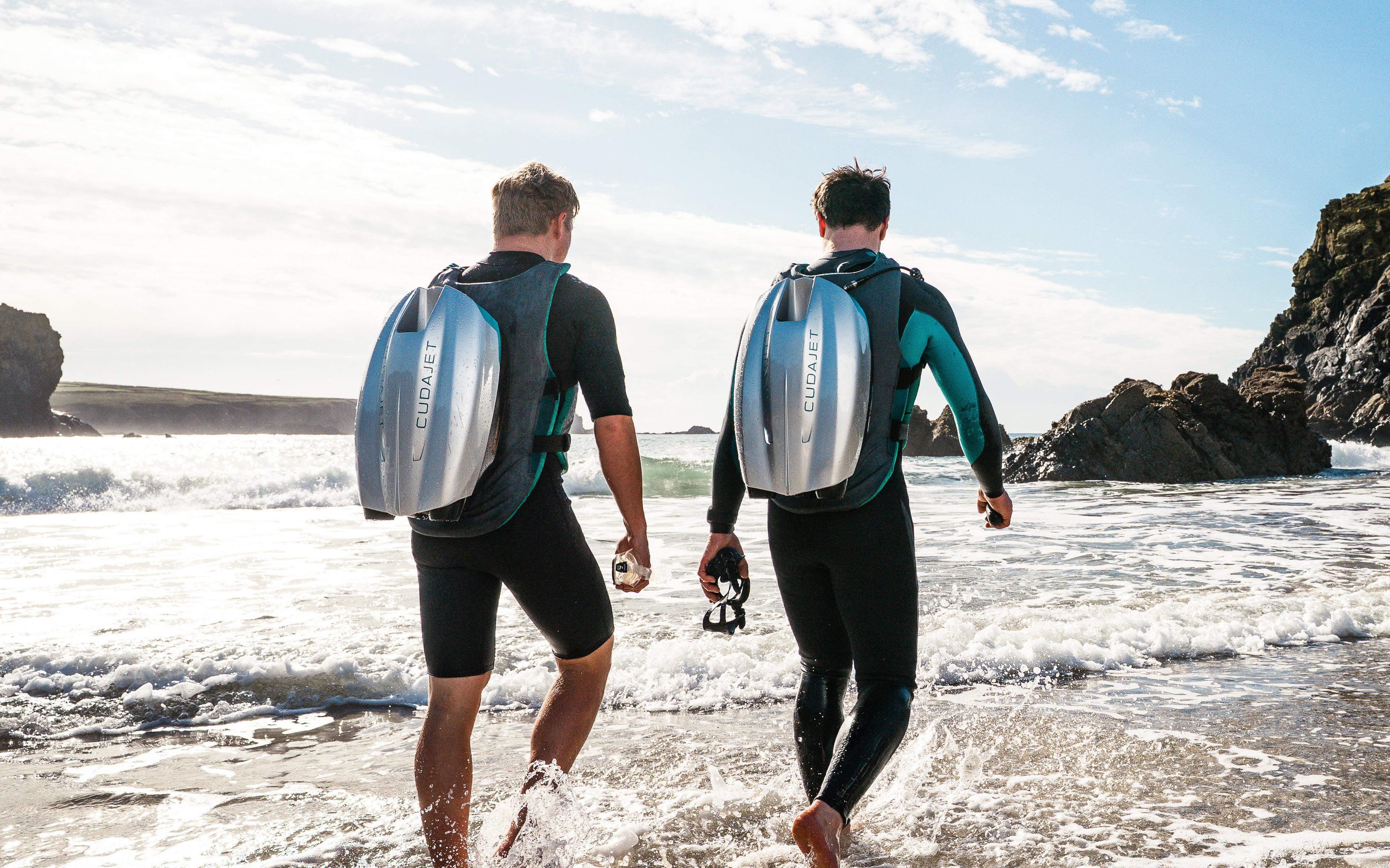 Two people walking into the sea with CudaJet on their backs