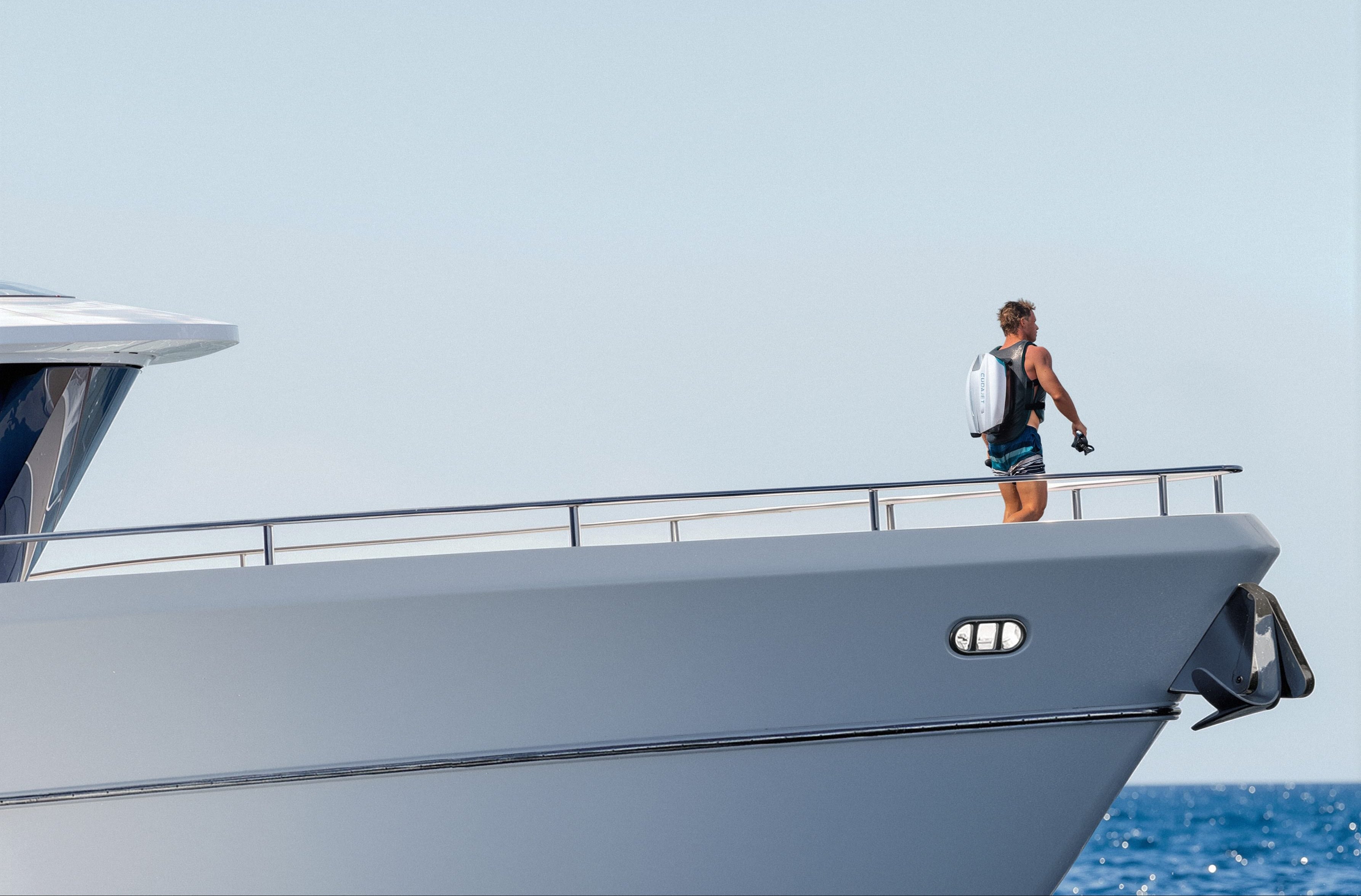 Person walking on the deck of a large yacht wearing a underwater jetpack