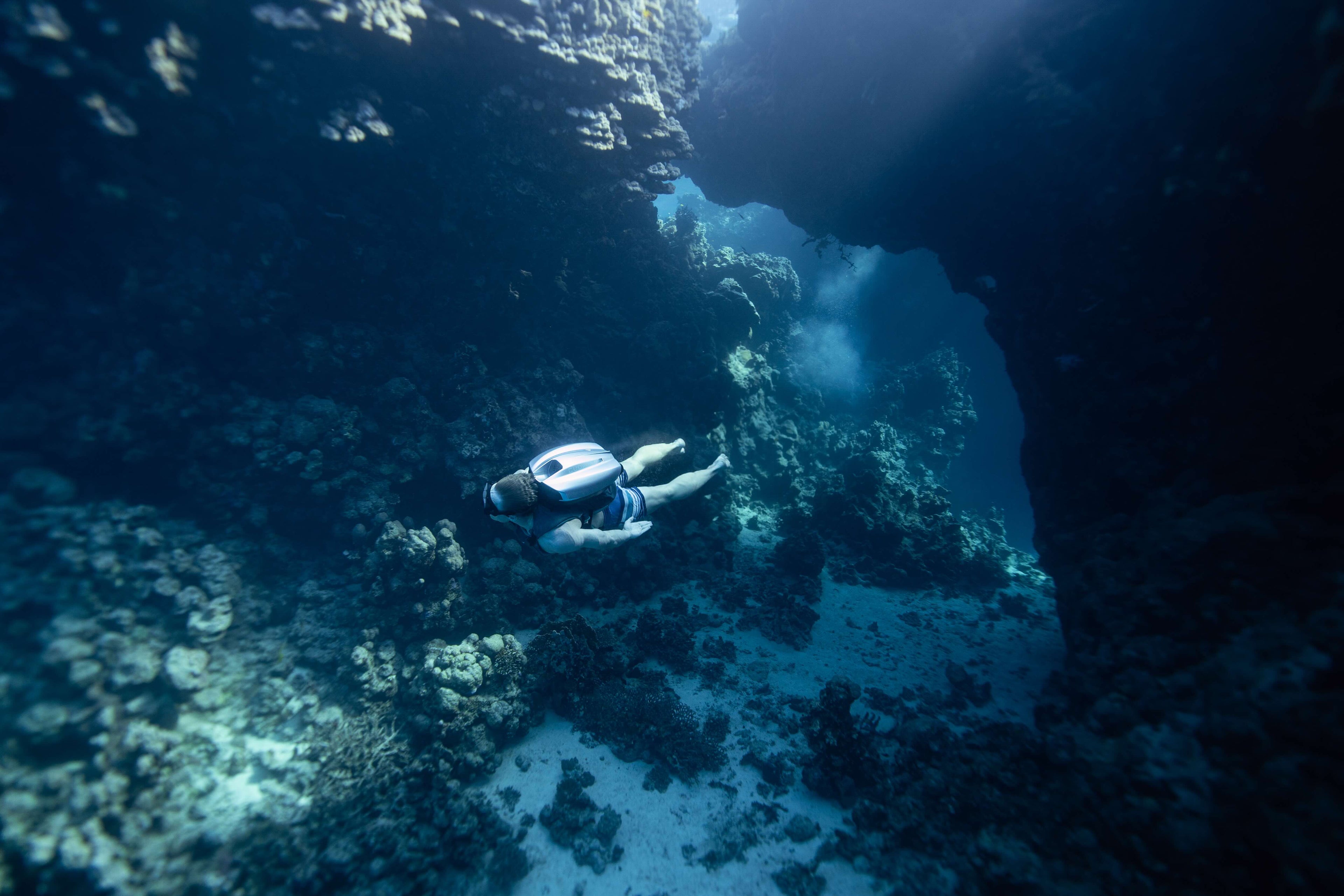 Person Jetpacking in a dark underwater cave with rocky walls and marine life.