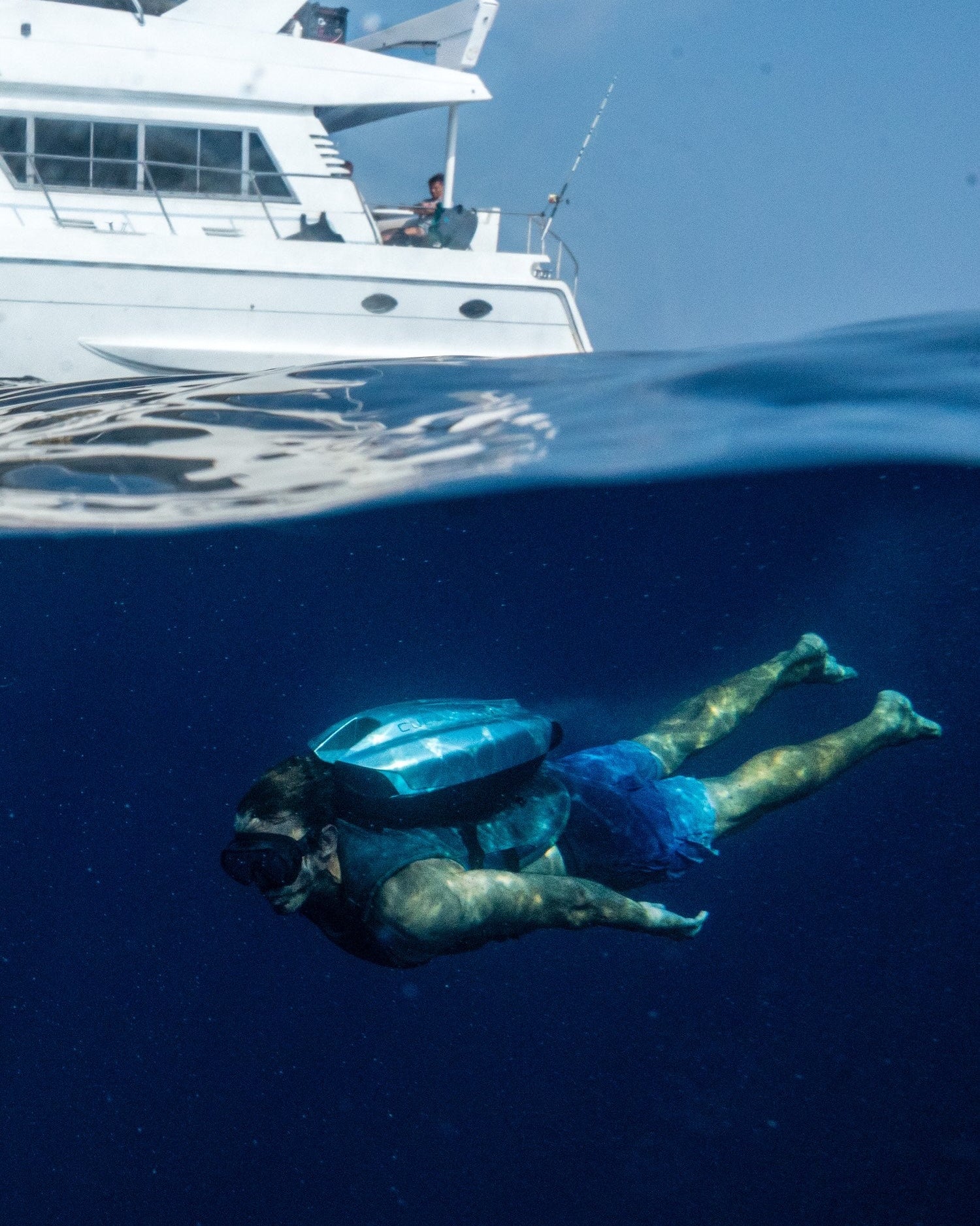 Person using underwater jetpack in clear blue water with a boat in the background