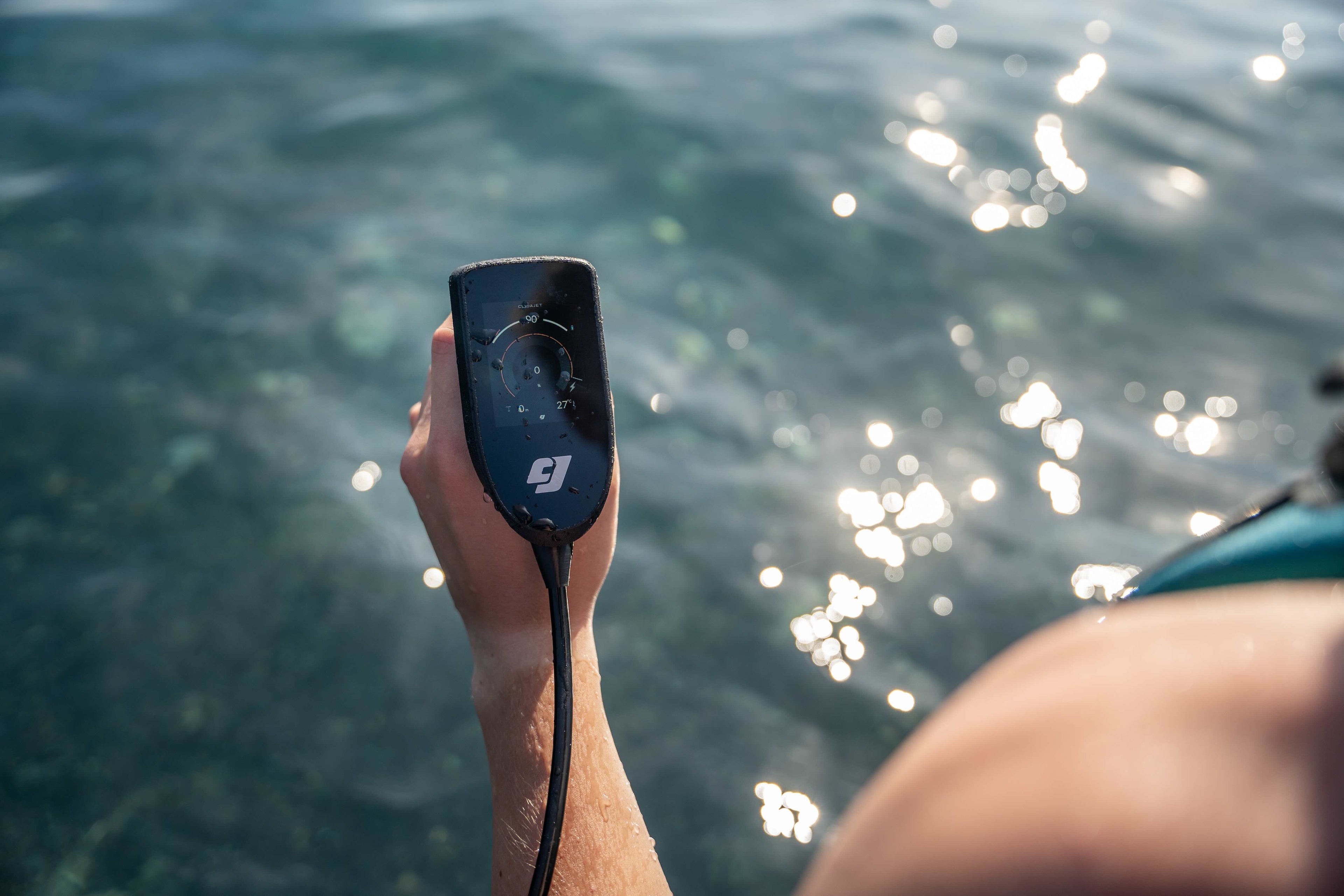 Hand holding a CudaJet underwater jetpack controller over water with sunlight reflecting on the surface